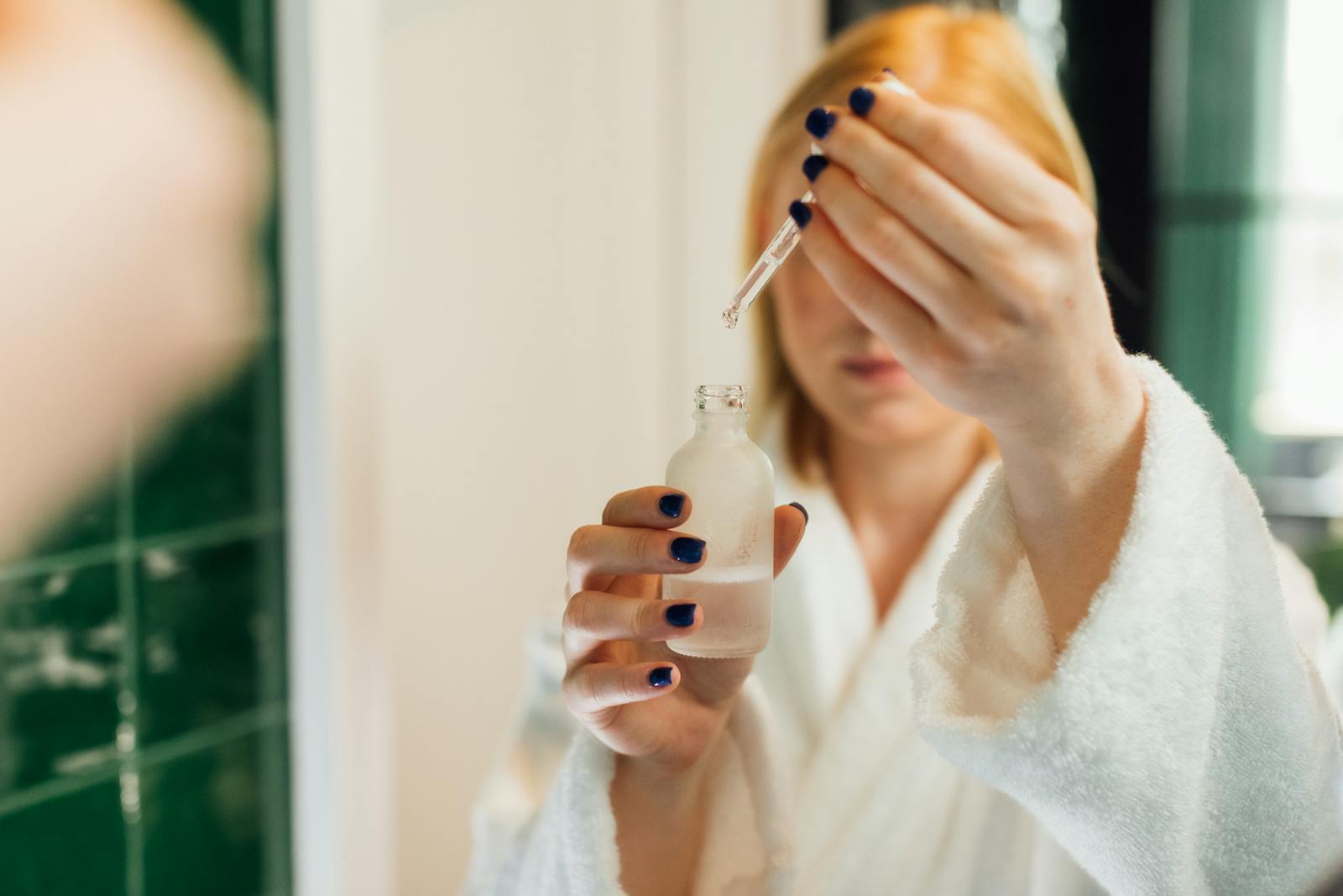 Woman holding a hyaluronic acid serum bottle in front of a bathroom mirror