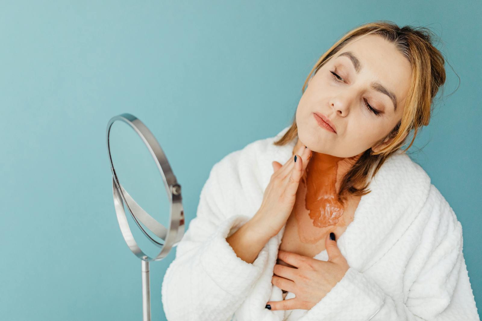 Woman applying salicylic acid BHA treatment to her face in front of a bathroom mirror