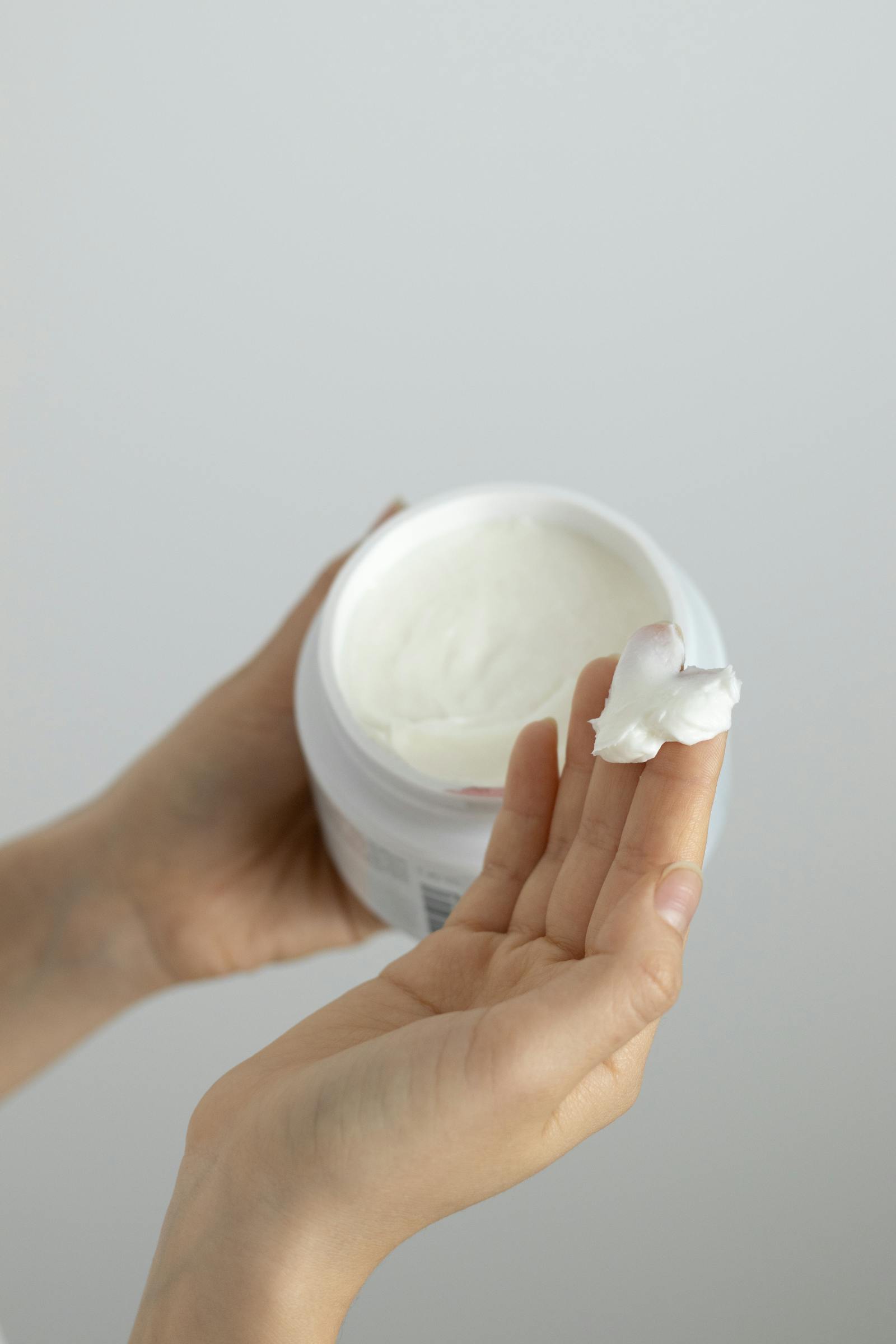 Hands smoothing a thin layer of petrolatum-based balm across the back of the hand, illustrating the slugging technique